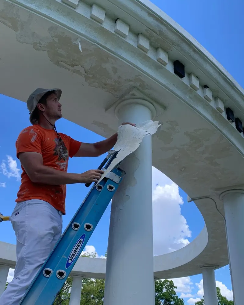 Great Dane painter on a ladder scraping a white column
